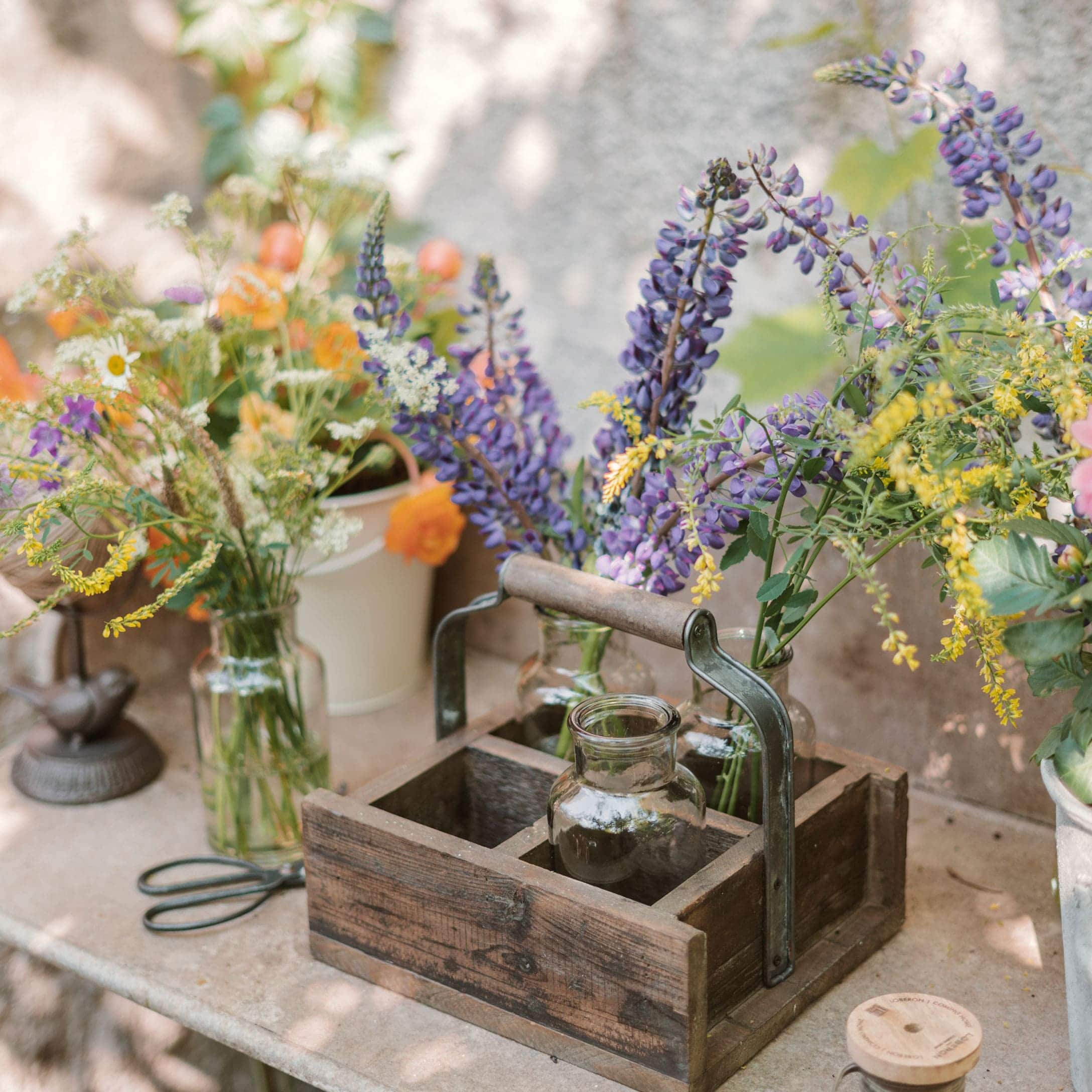 Organizador de madera con asa y jarrones de vidrio con flores de colores sobre mesa de jardín