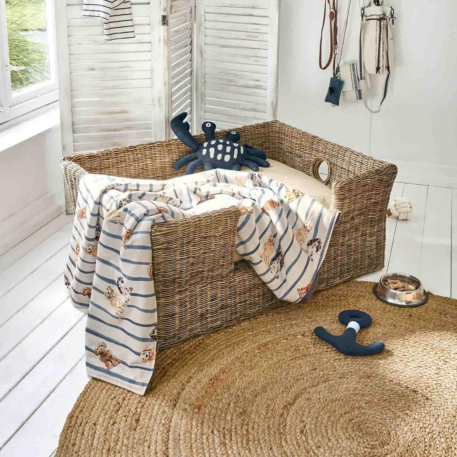 Cama de mimbre para perro con cojín beige, manta a rayas con diseño de perros, juguetes y cuenco