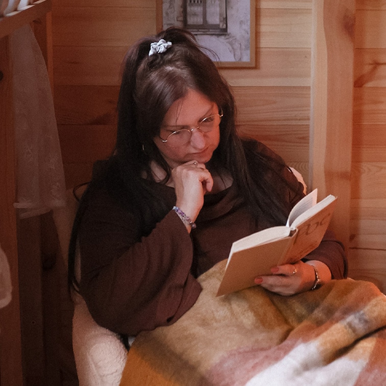 Mujer leyendo un libro bajo una manta suave multicolor en un interior de madera, momento de relax