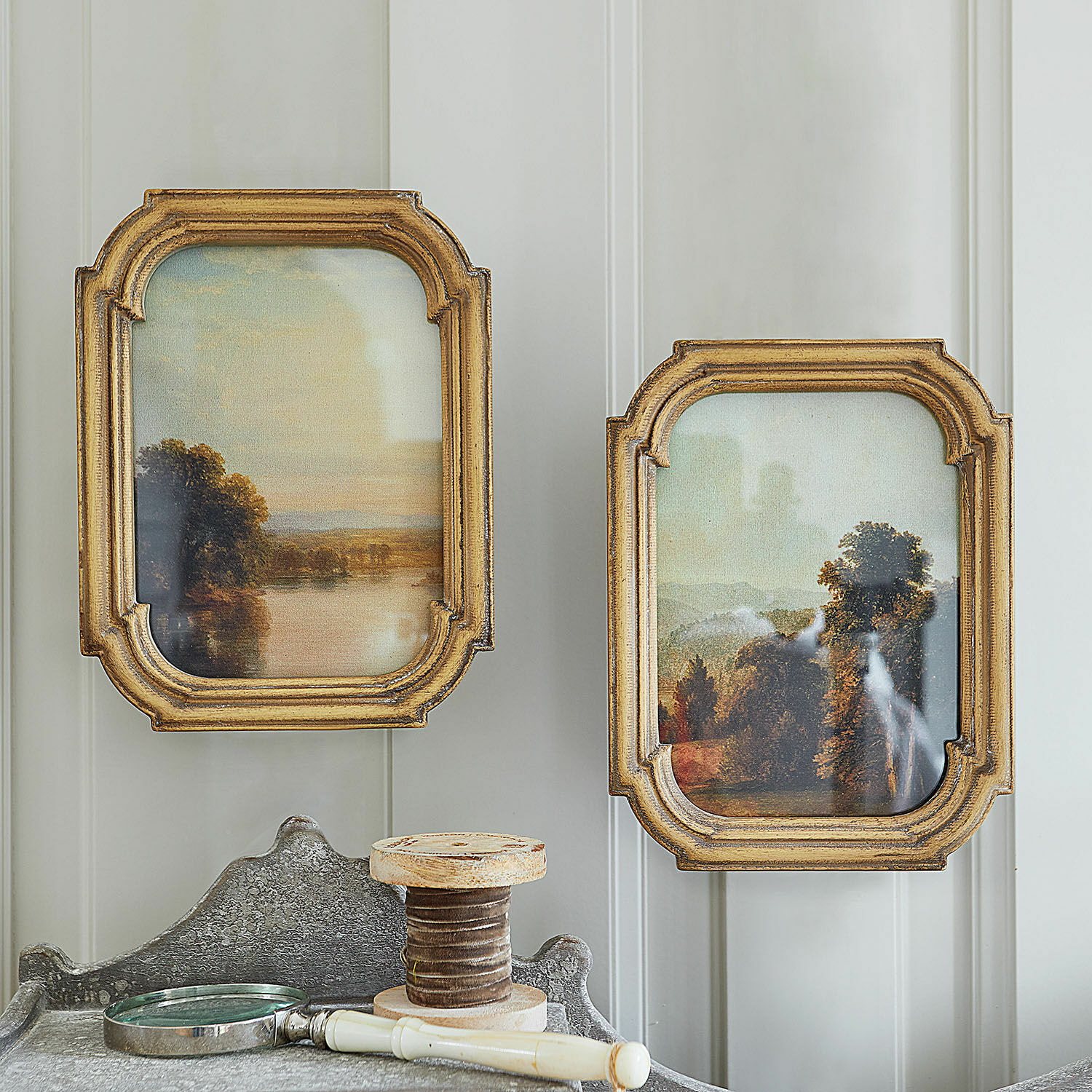 Set de 2 cuadros Fleuroix Dos cuadros de paisaje en marcos de madera dorada sobre pared clara, decoración vintage