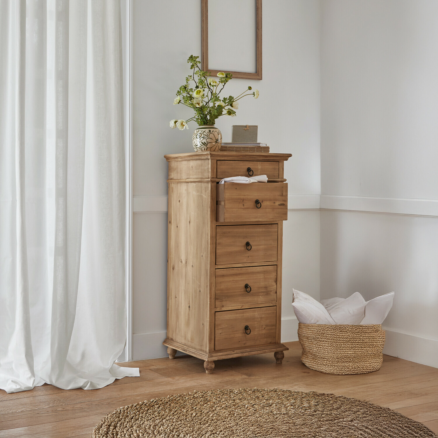 Cómoda alta de madera de pino natural con cuatro cajones y jarrón decorativo con flores en interior luminoso