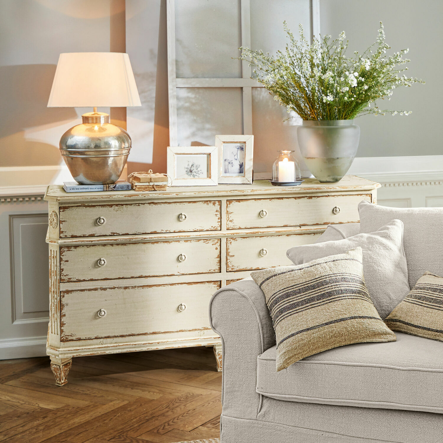 Cómoda Commeren Cómoda de madera crema estilo vintage con lámpara, marcos y decoraciones en sala con sofá beige