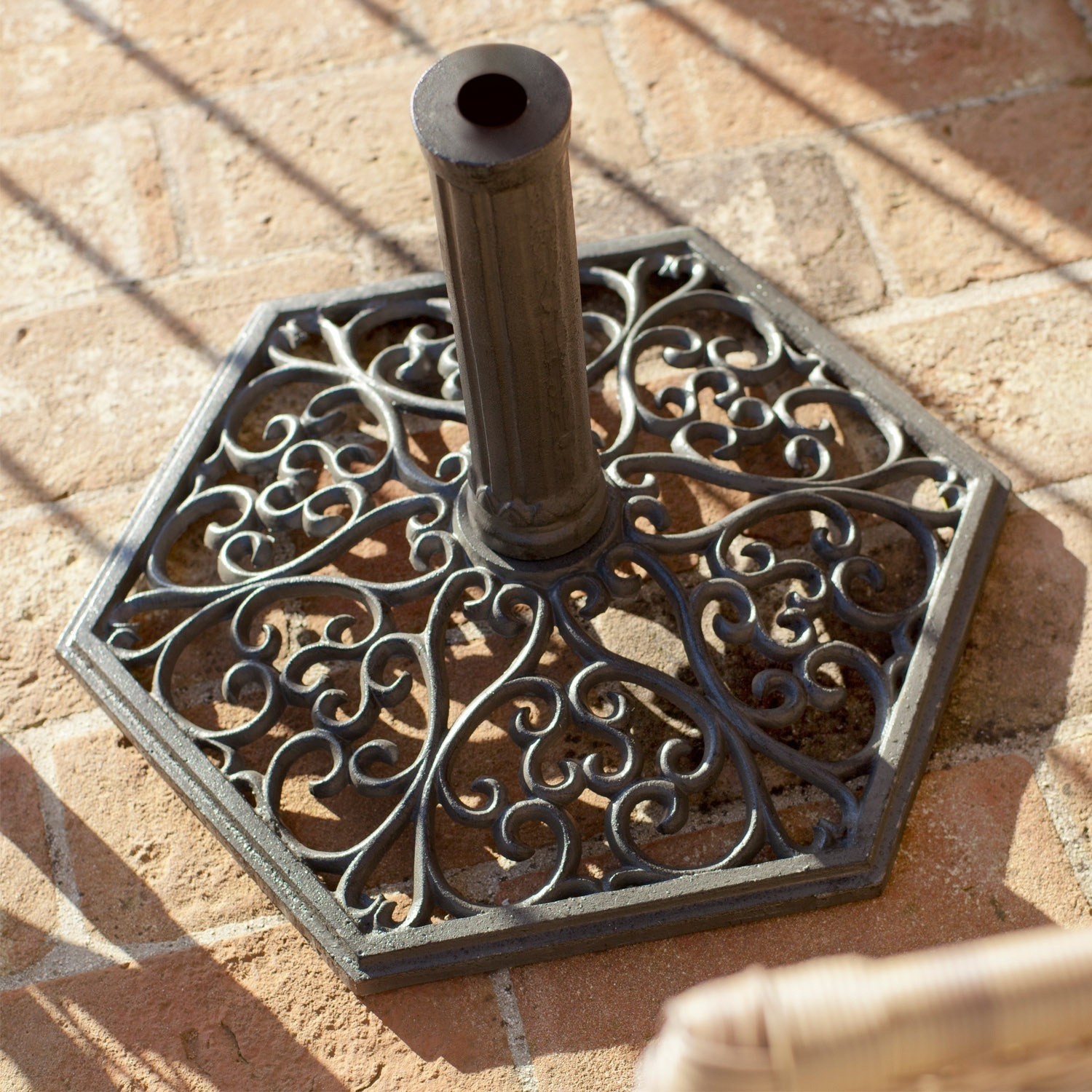 Paragüero Montant Base de sombrilla de metal negro con diseño decorativo sobre suelo de ladrillo, estable y duradera