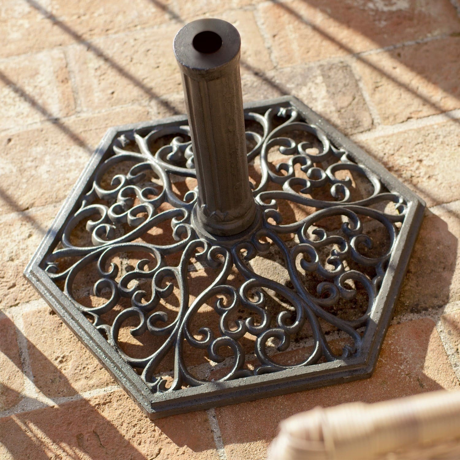 Paragüero Montant Base de sombrilla de metal negro con diseño decorativo sobre suelo de ladrillo, estable y duradera