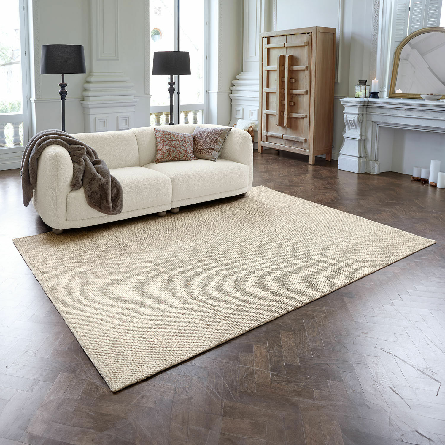 Alfombra Coleman Alfombra beige de material natural sobre suelo de madera oscura en salón elegante con sofá crema