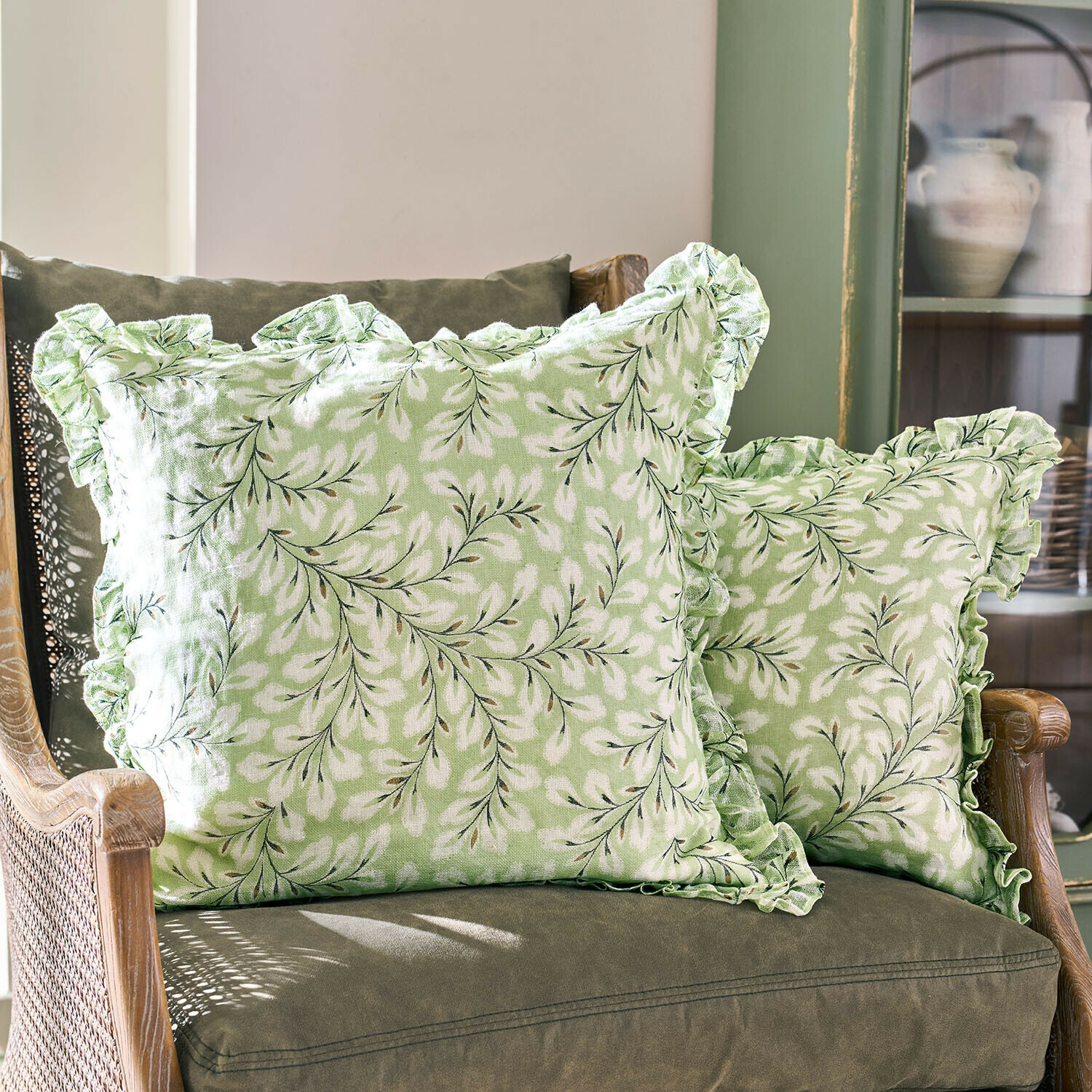 Set de 2 fundas de cojín Norelline Cojines verdes con estampado de hojas blancas y volantes en sillón verde, textiles para salón