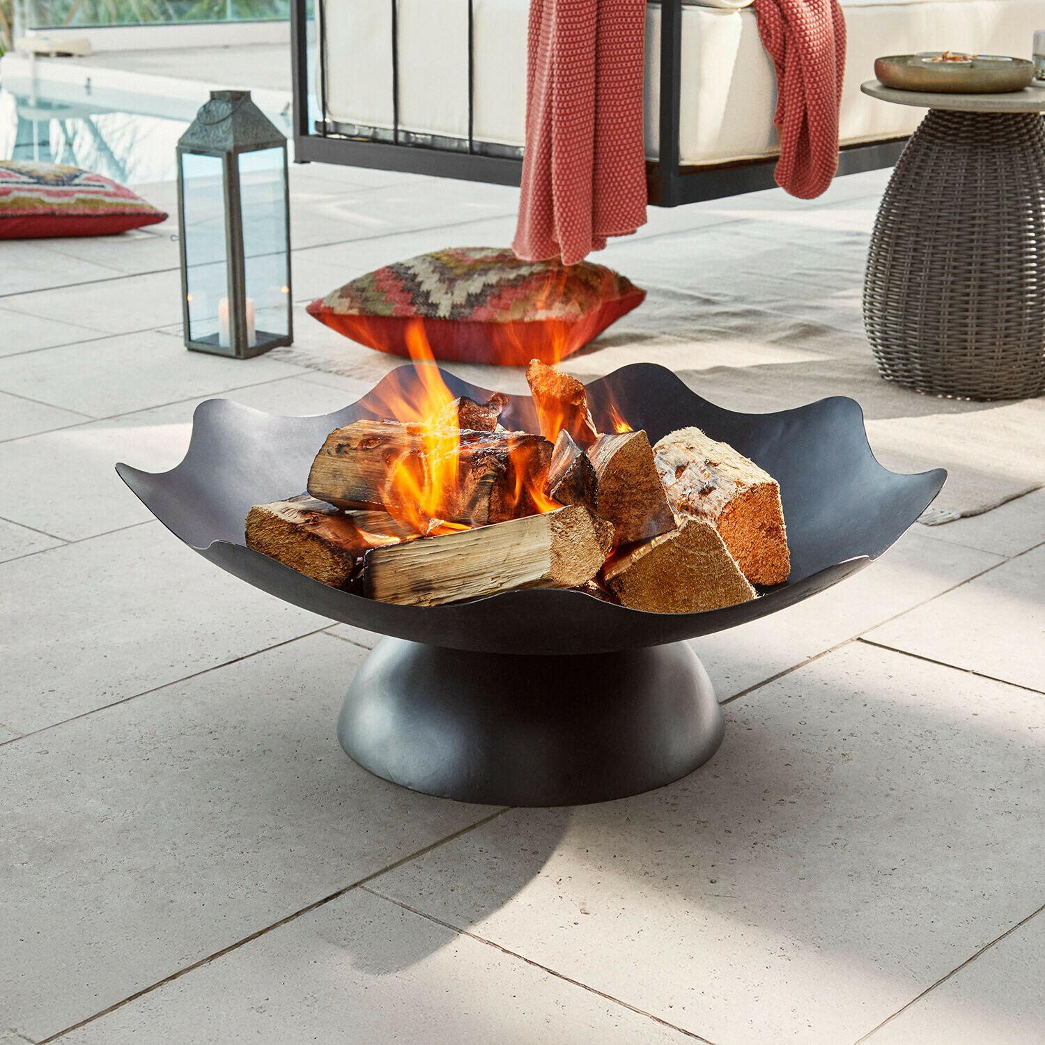 Brasero Ironwell Brasero metálico negro con leña ardiendo en terraza, ideal para jardín y momentos al aire libre
