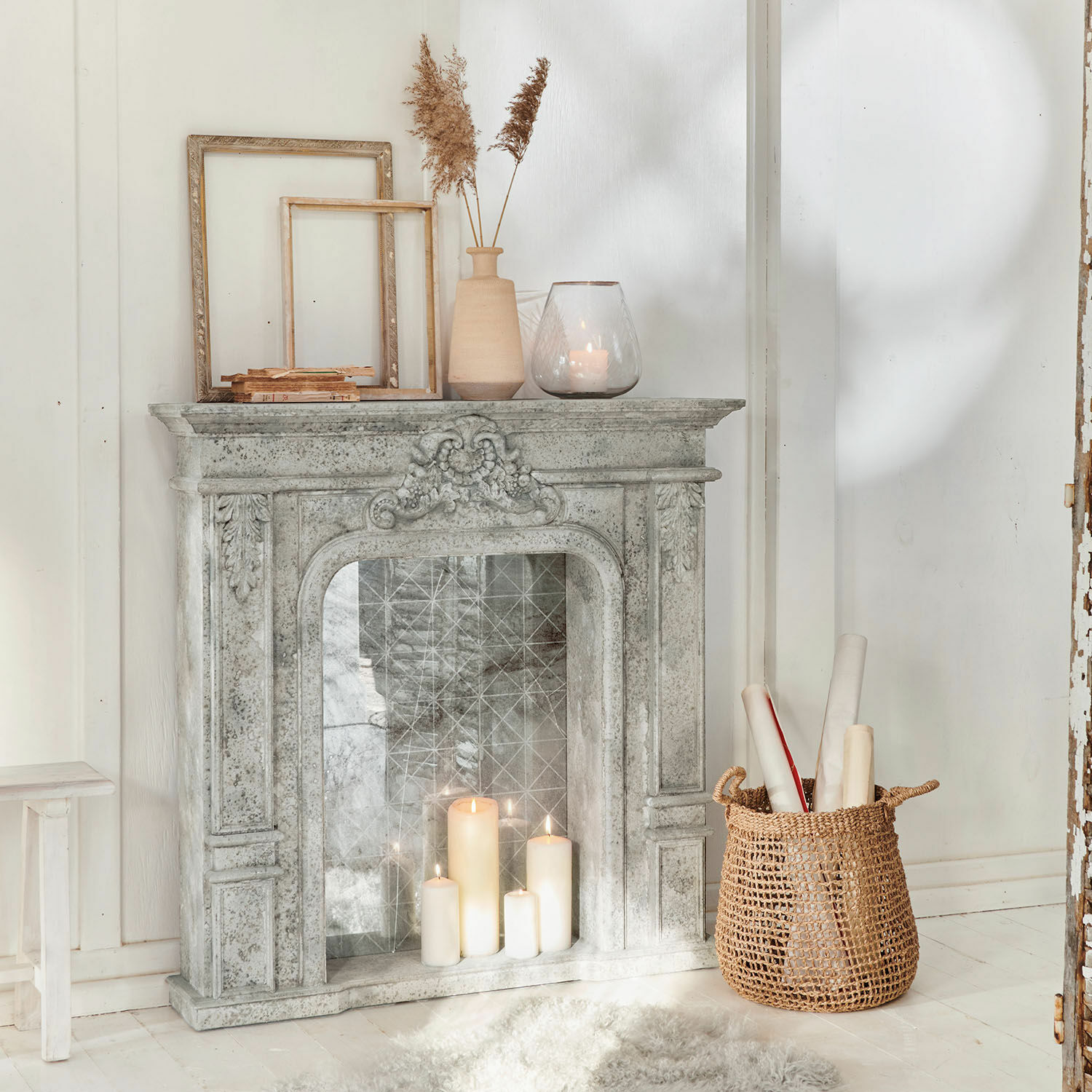 Consola de chimenea Rethonvillers Chimenea decorativa de piedra gris con velas encendidas y cesta de mimbre sobre suelo blanco