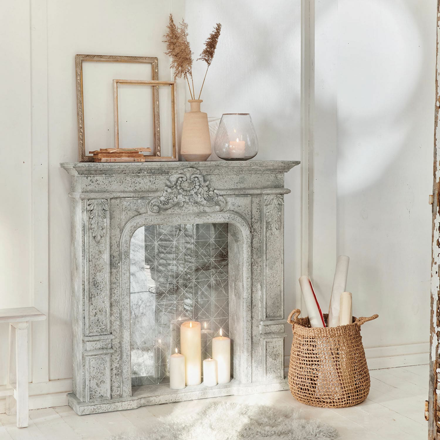 Consola de chimenea Rethonvillers Chimenea decorativa de piedra gris con velas encendidas y cesta de mimbre sobre suelo blanco
