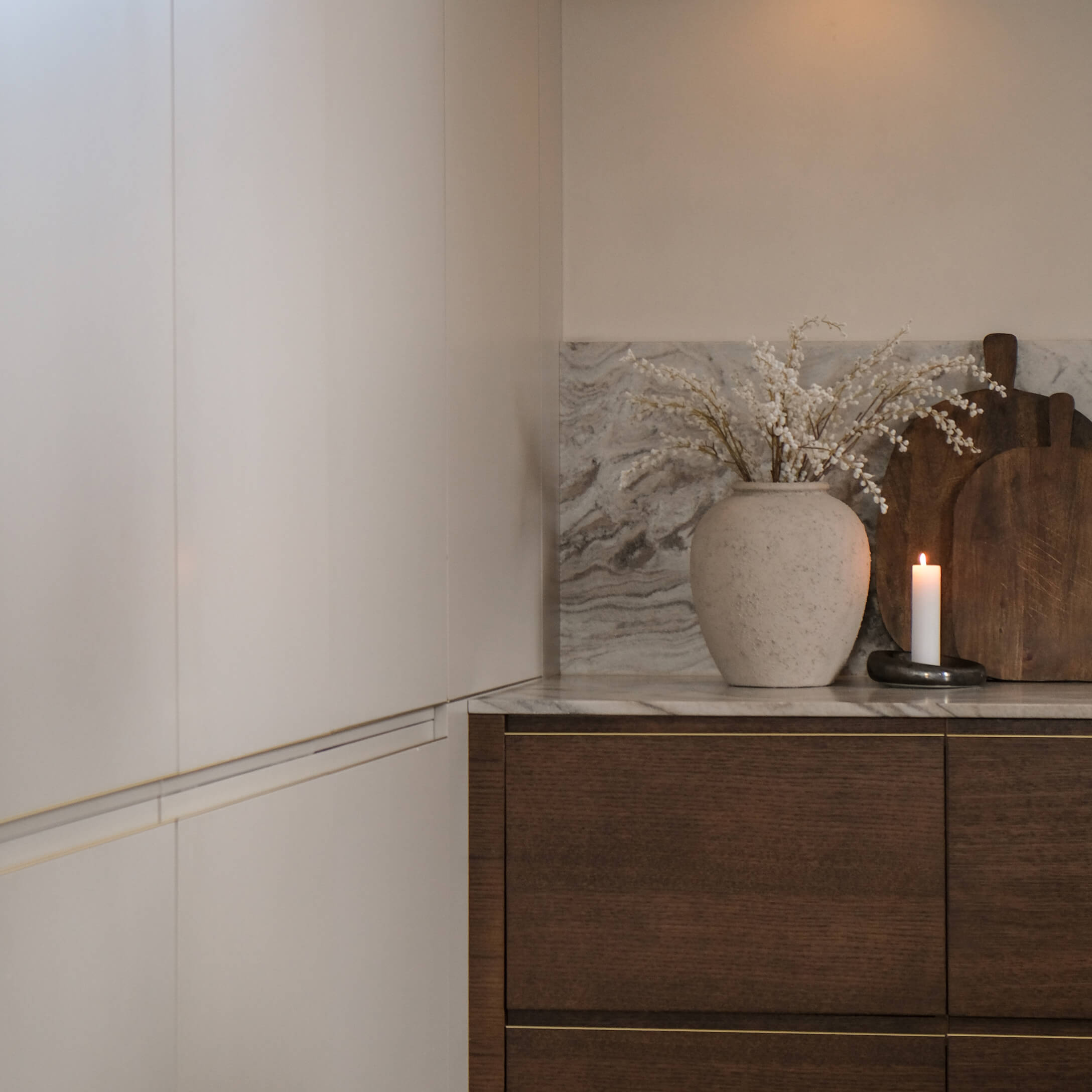 Cocina con armarios blancos, encimera de mármol, jarrón decorativo con flores blancas y vela encendida