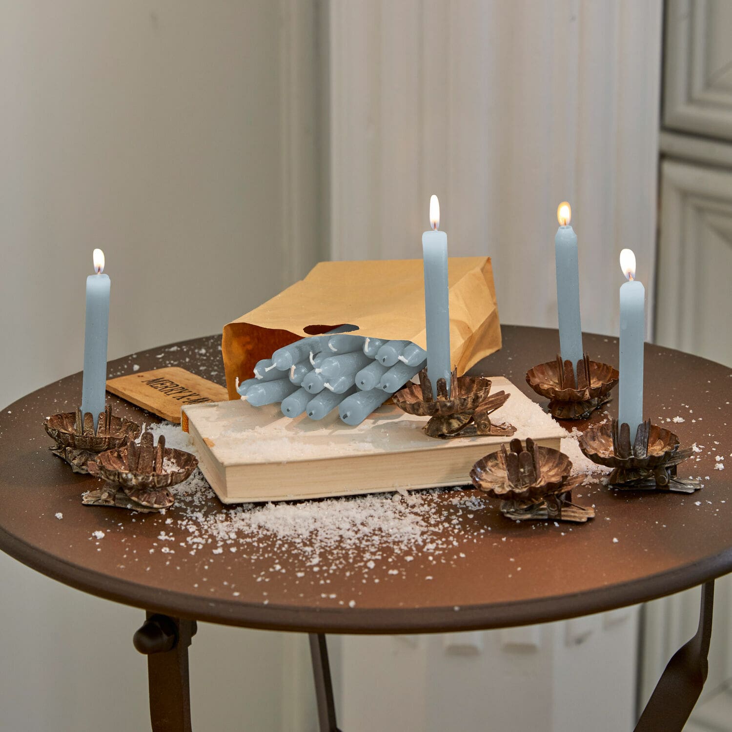 Set de 20 velas Noufa Velas azules con candelabros de metal sobre mesa marrón con libro y bolsa de papel