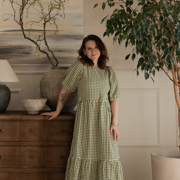 Mujer con vestido verde a cuadros junto a cómoda de madera en interior acogedor con plantas