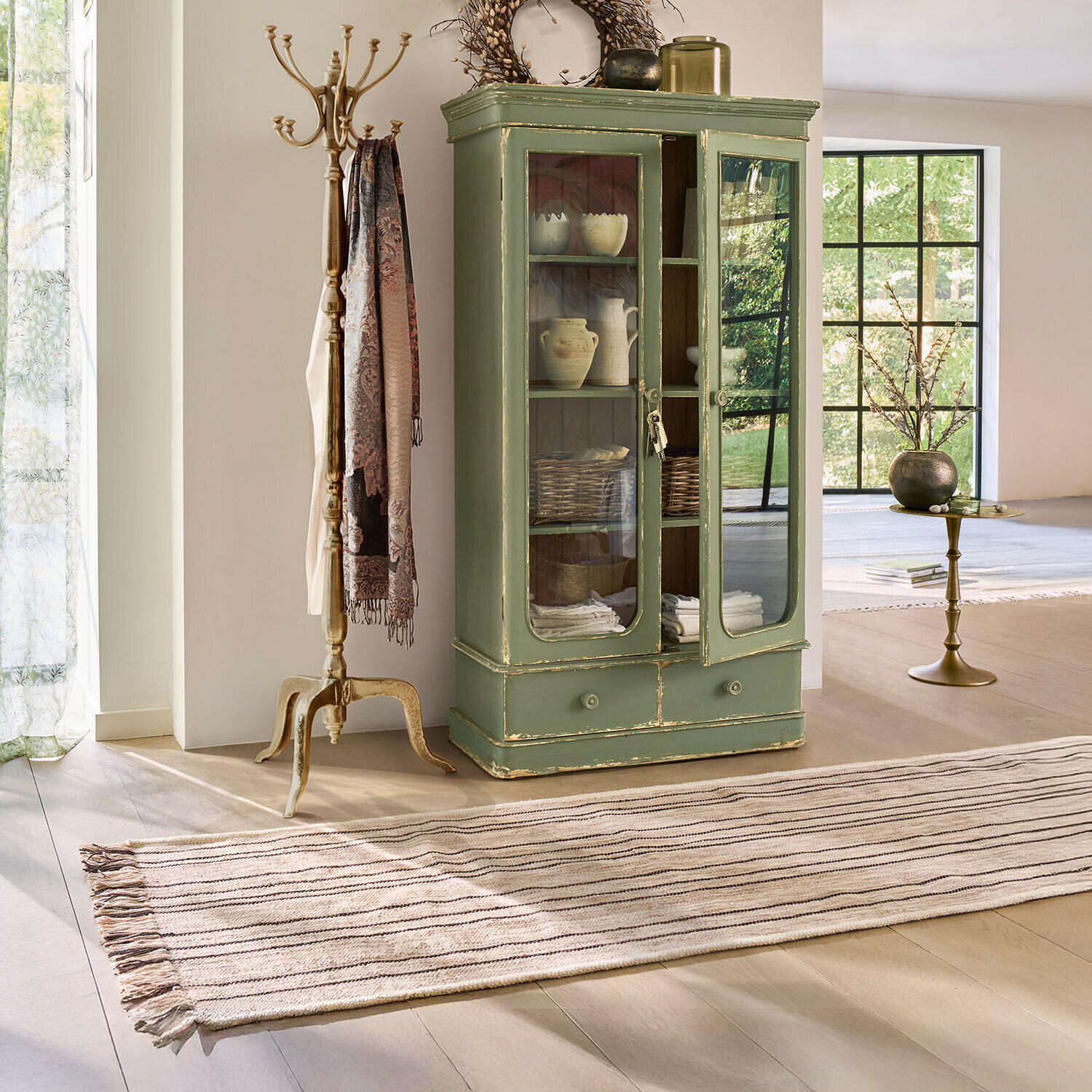 Alfombra Brisalda Vitrina de madera verde con puertas de cristal y cajón en salón luminoso de estilo vintage