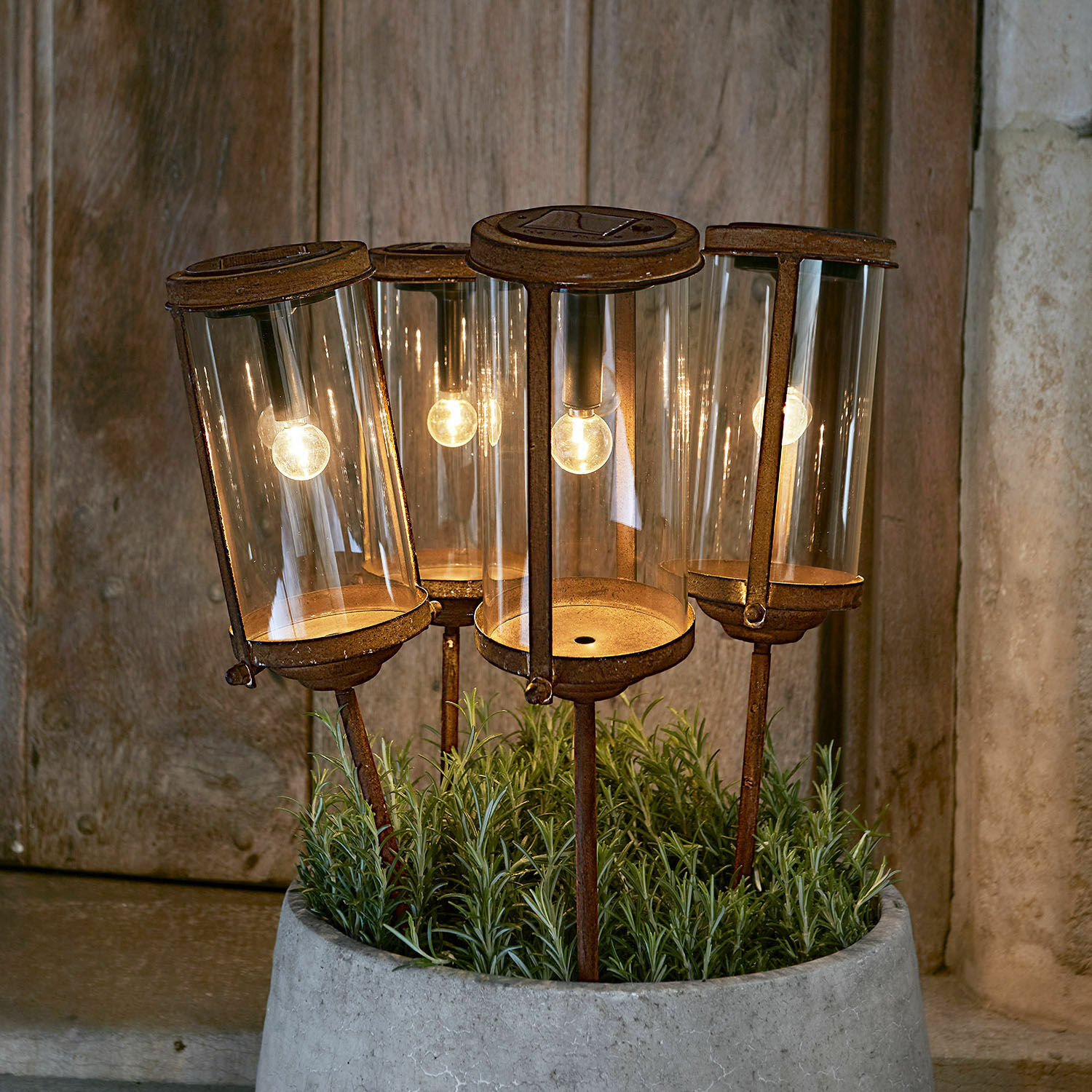 Farol solar Conjunto de cuatro faroles de jardín oxidados con pantalla de vidrio y luz LED cálida en maceta de cemento