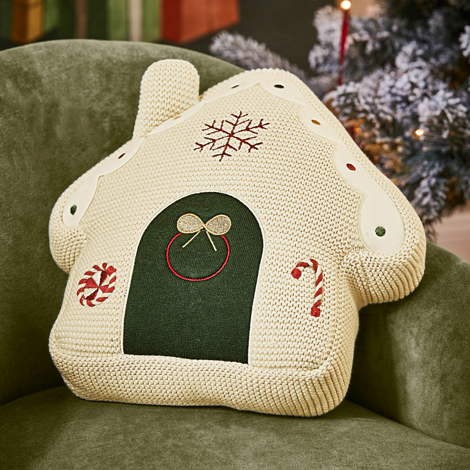 Casa de tela estilo pan de jengibre Skavari Cojín decorativo en forma de casa de punto crema con motivos navideños y detalles verdes sobre sillón verde