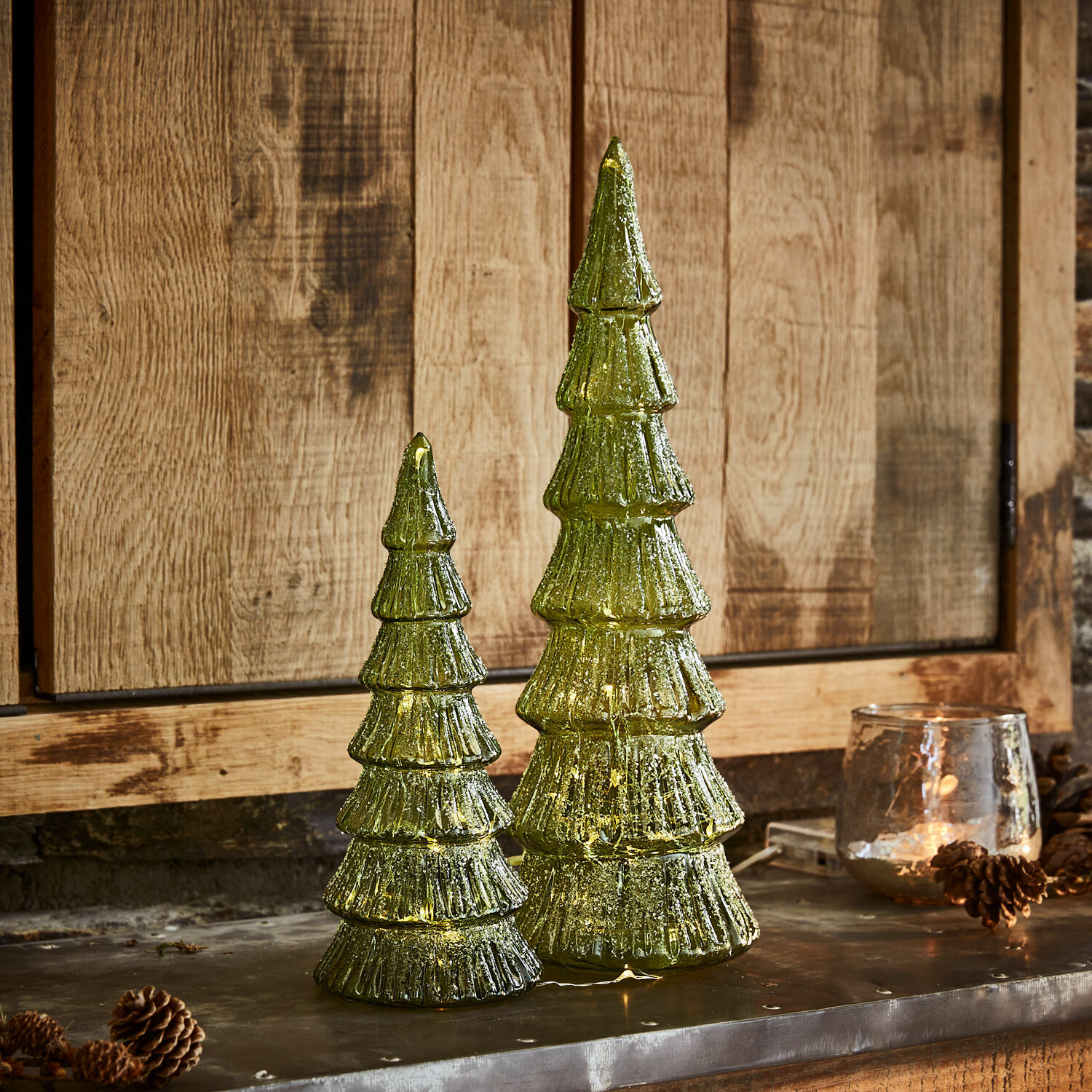 Set de 2 árboles LED Merrton Dos decoraciones navideñas de árbol de vidrio verde con luces LED sobre fondo de madera, adornos festivos