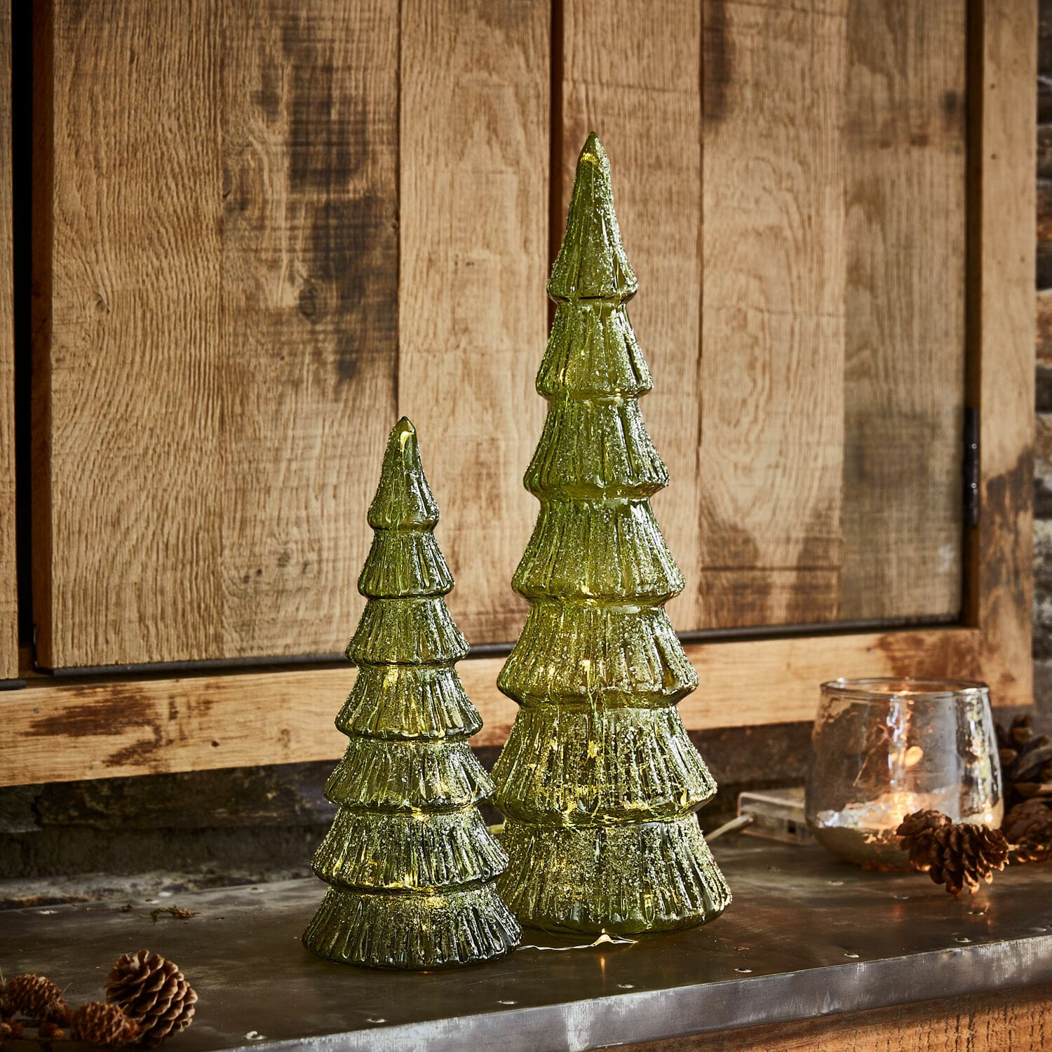 Set de 2 árboles LED Merrton Dos decoraciones navideñas de árbol de vidrio verde con luces LED sobre fondo de madera, adornos festivos