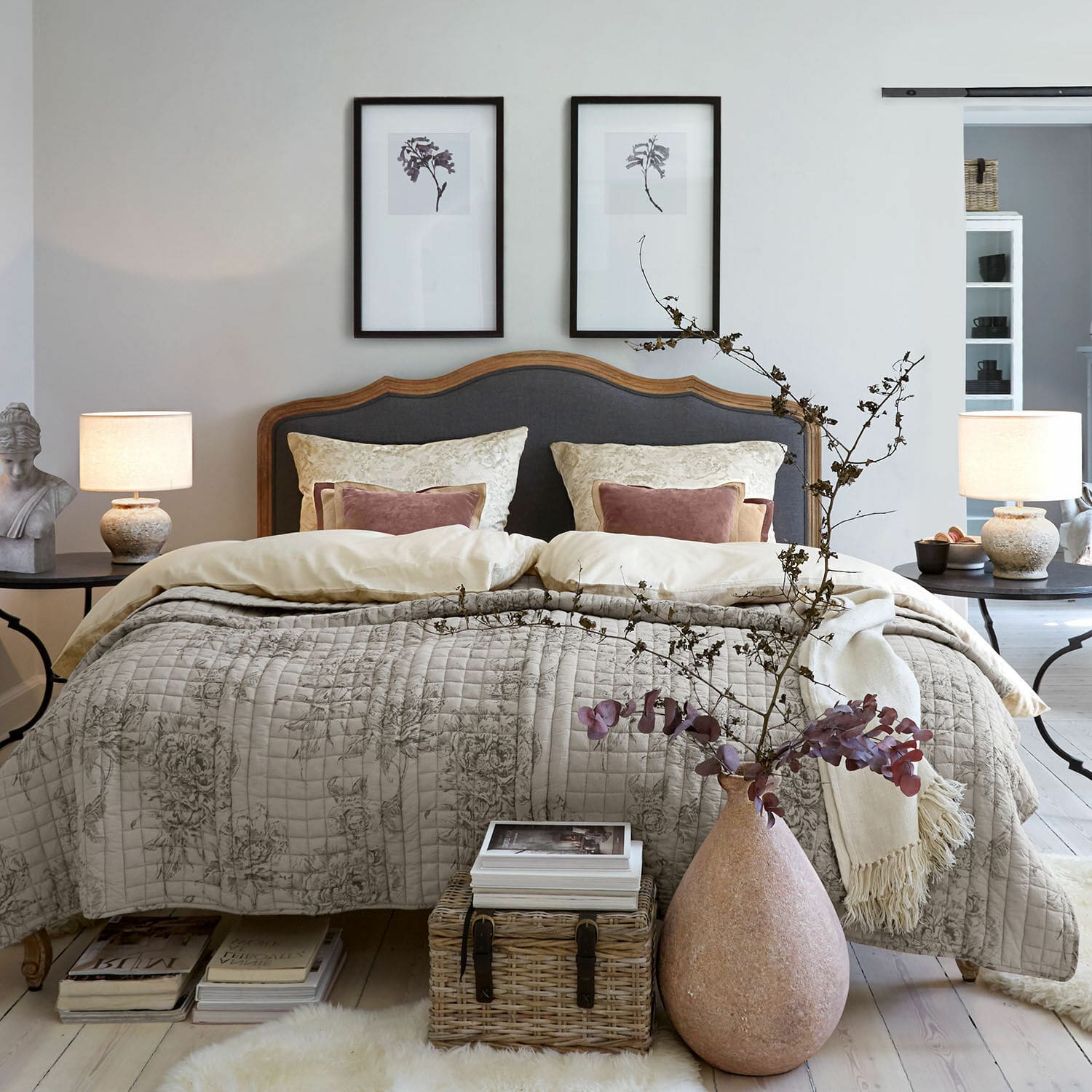 Ropa de cama Bravonea Dormitorio acogedor con cama de cabecero de madera y tapizado gris, colcha beige con diseño floral, decoración natural