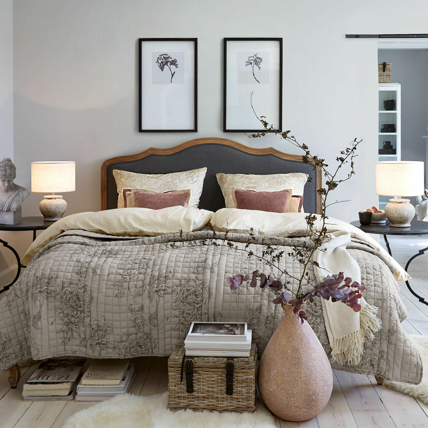 Ropa de cama Bravonea Dormitorio acogedor con cama de cabecero de madera y tapizado gris, colcha beige con diseño floral, decoración natural