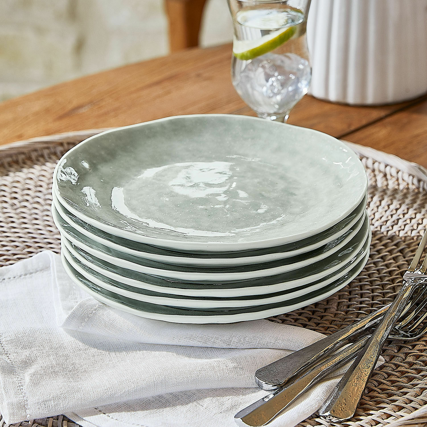 Set de 6 platos de postre Braganza Conjunto de seis platos de cerámica gris sobre bandeja de mimbre con cubiertos metálicos
