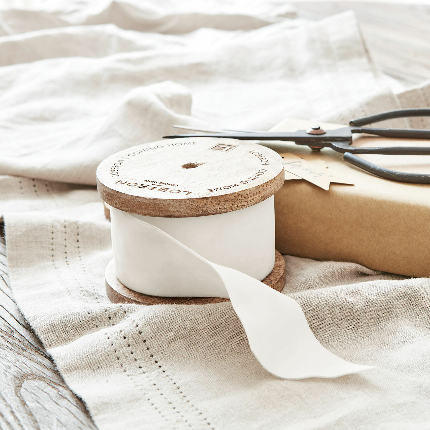 Cinta blanca de algodón en carrete de madera con texto Loberon sobre tela de lino, accesorios de decoración y embalaje