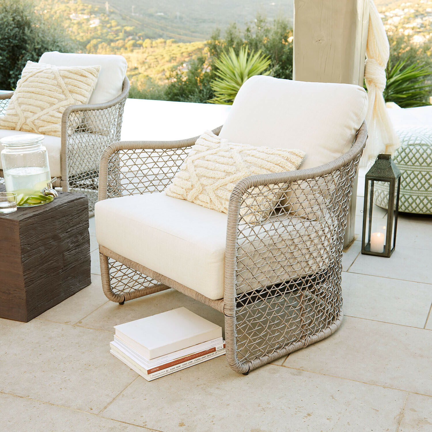 Sillón Langforda Sillón de jardín de ratán beige con cojín crema en terraza con vistas a la naturaleza