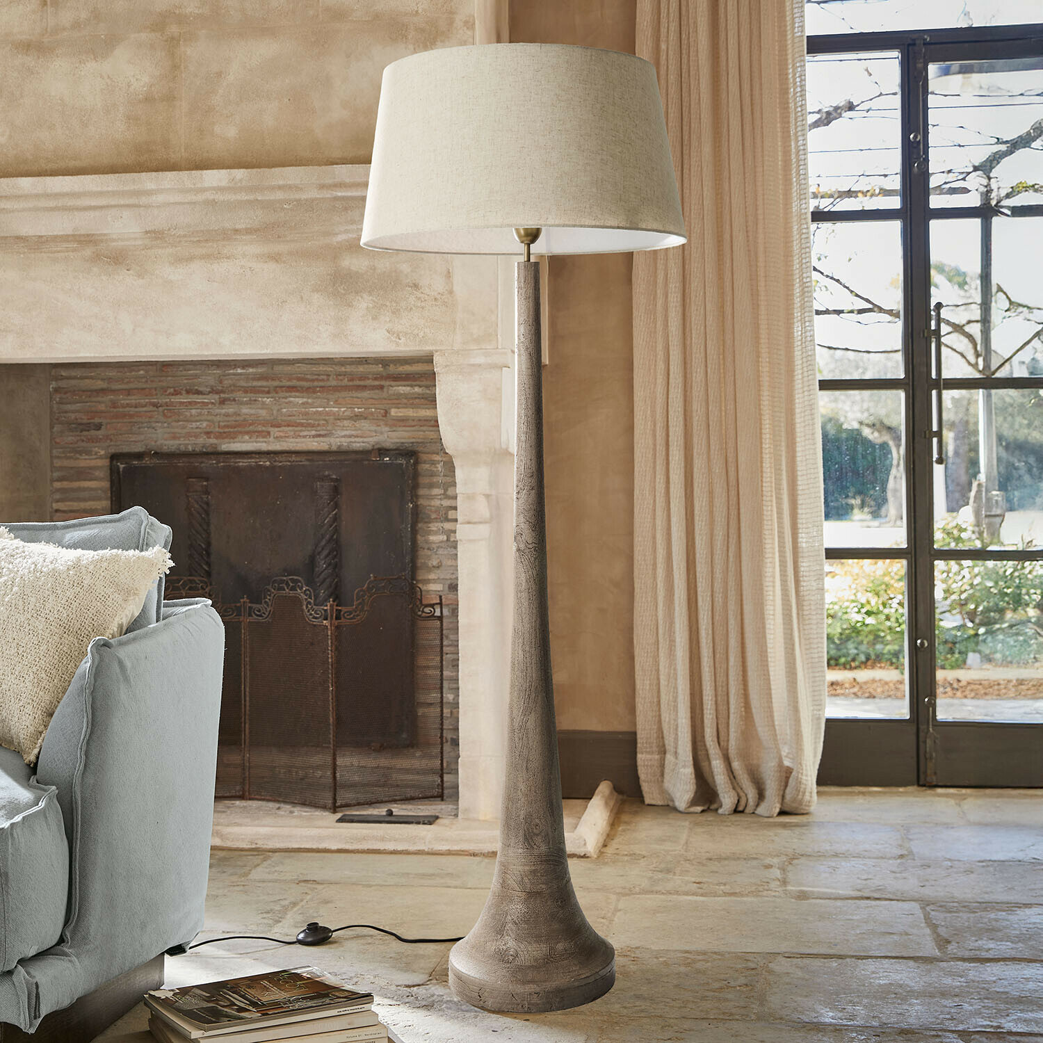 Lámpara de pie con base de madera y pantalla beige en salón acogedor con chimenea y sofá azul
