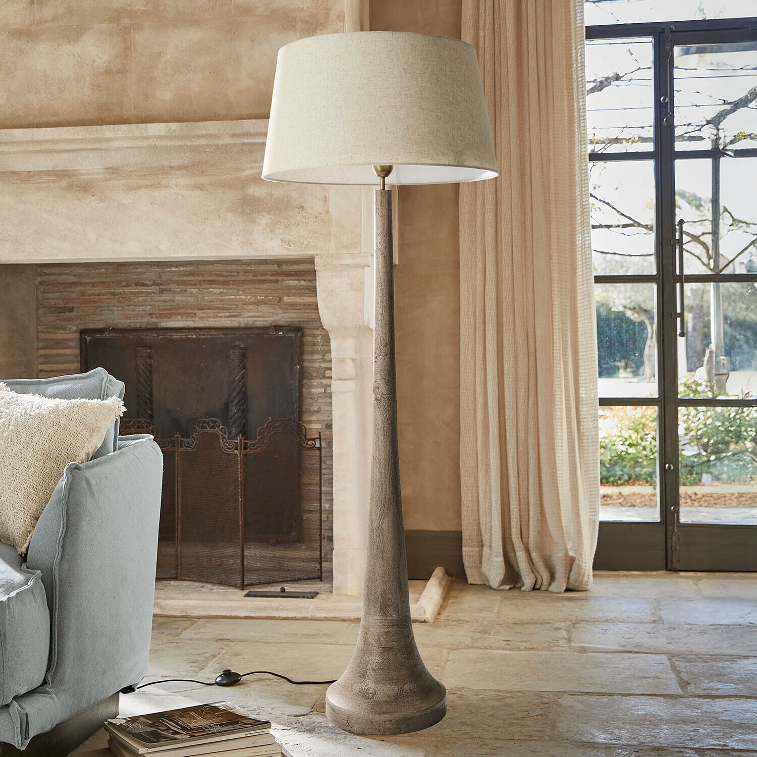 Lámpara de pie Helsfjord Lámpara de pie con base de madera y pantalla beige en salón acogedor con chimenea y sofá azul