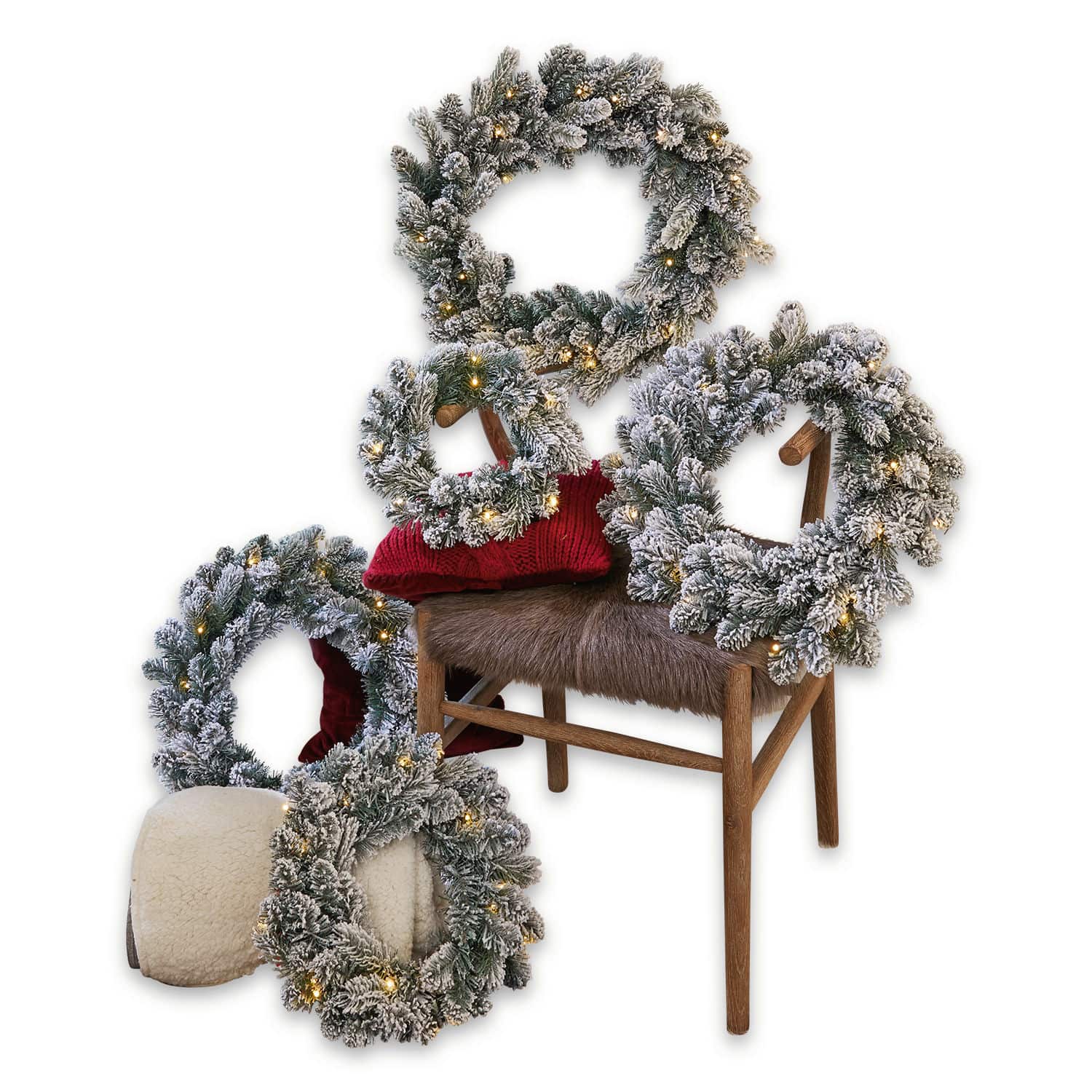 Set de 5 coronas Ellaria Conjunto de cinco coronas navideñas con ramas nevadas y luces LED cálidas sobre silla y cojín