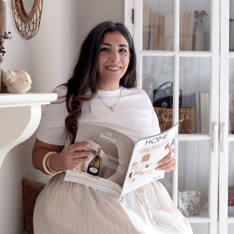 Mujer con camiseta blanca y falda clara leyendo revista de decoración en habitación luminosa con armario de madera