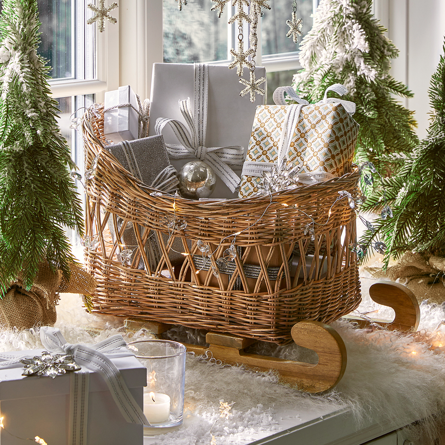 Trineo de mimbre con patines de madera lleno de regalos envueltos en plata y blanco para decoración navideña