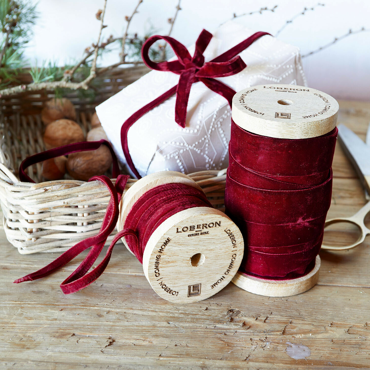 Set de 2 cintas de terciopelo Liandis Dos carretes de madera con cinta de terciopelo burdeos sobre mesa de madera con tijeras y regalo