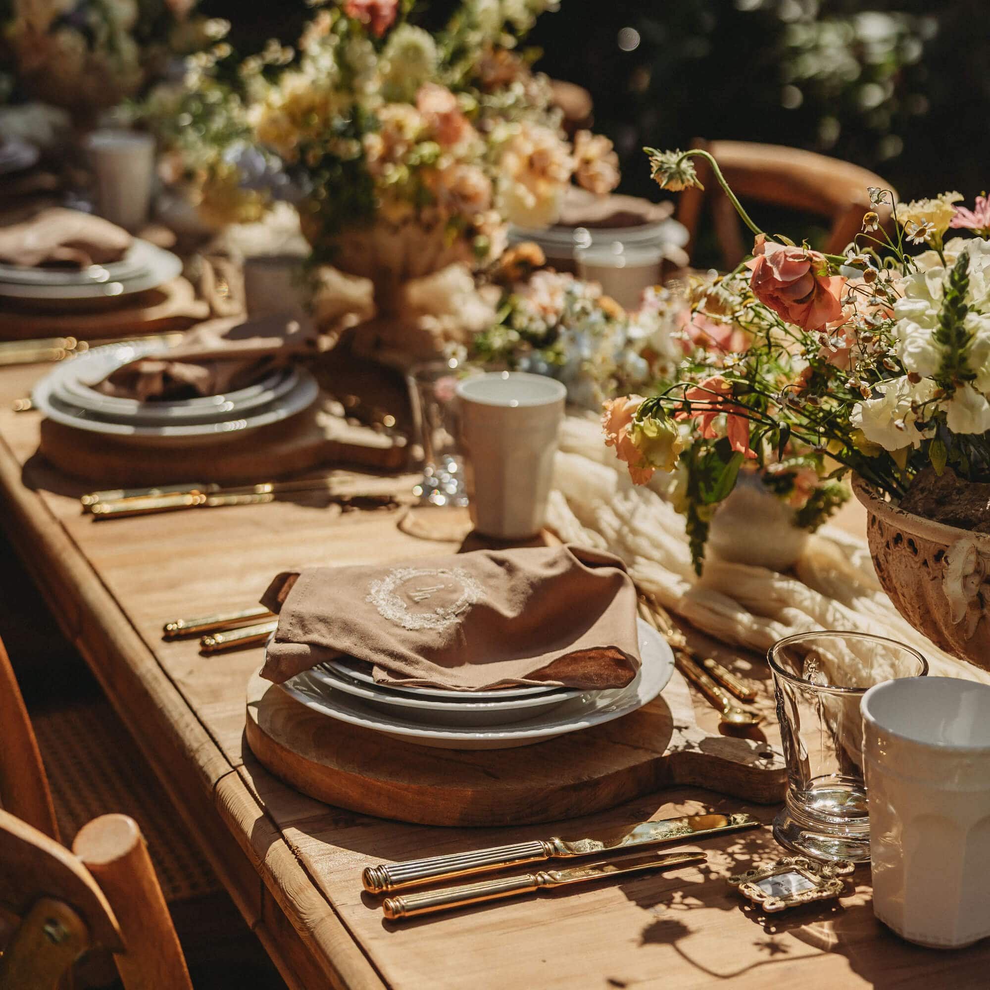 Mesa rústica de madera con vajilla, cubiertos dorados y decoración floral para evento especial