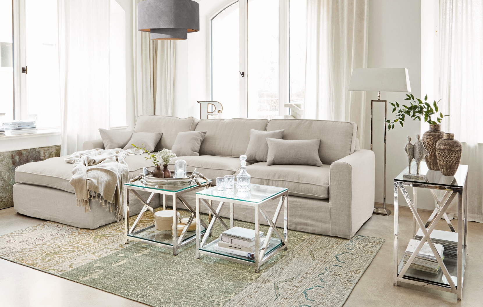 Sofá clásico beige de lino con cojines y mesas de cristal con estructura metálica en salón elegante