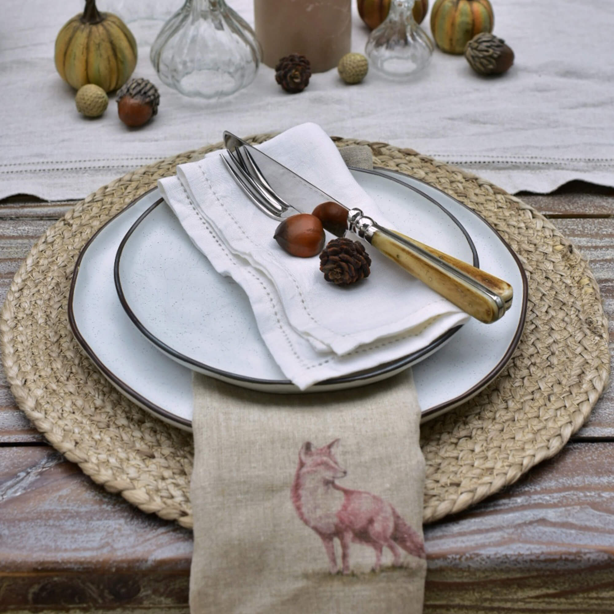 Juego de mesa con vajilla de cerámica blanca, cubiertos con mango de madera clara y servilleta de lino con estampado de zorro