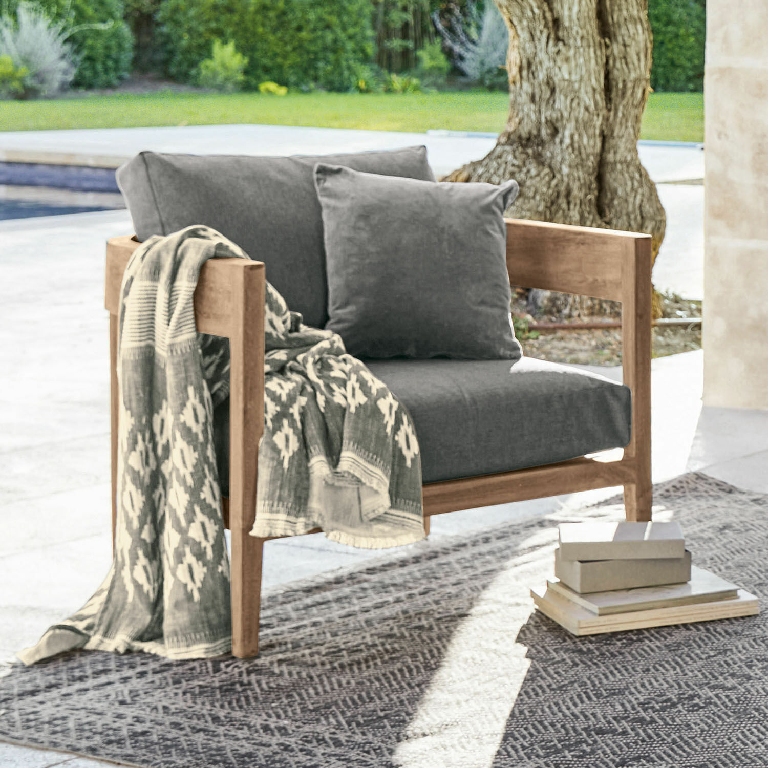 Sillón con estructura de madera y cojines grises, con manta estampada en exterior