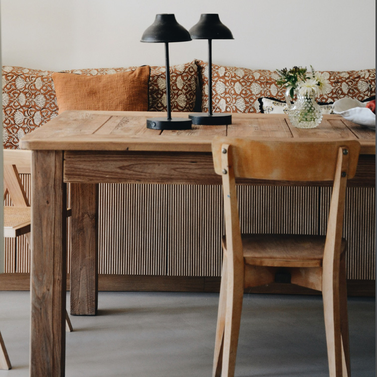 Mesa de madera con dos lámparas negras y flores en jarrón frente a sofá con cojines naranjas