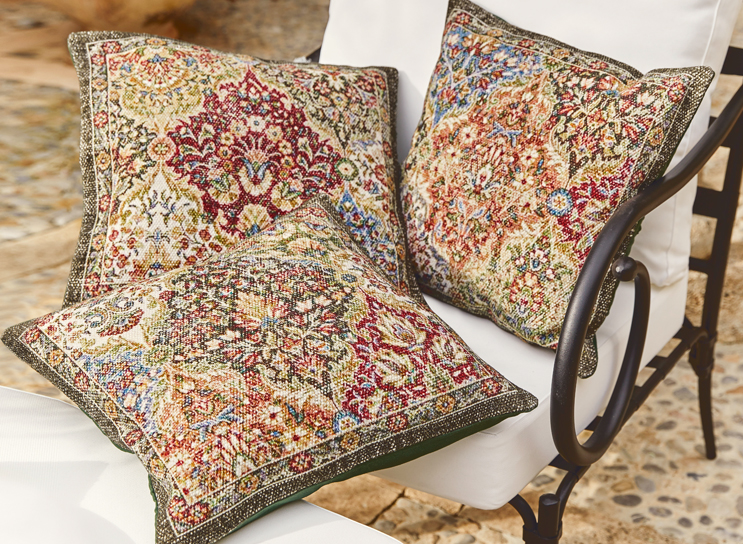 Tres cojines decorativos con diseño oriental en colores cálidos sobre silla blanca de metal