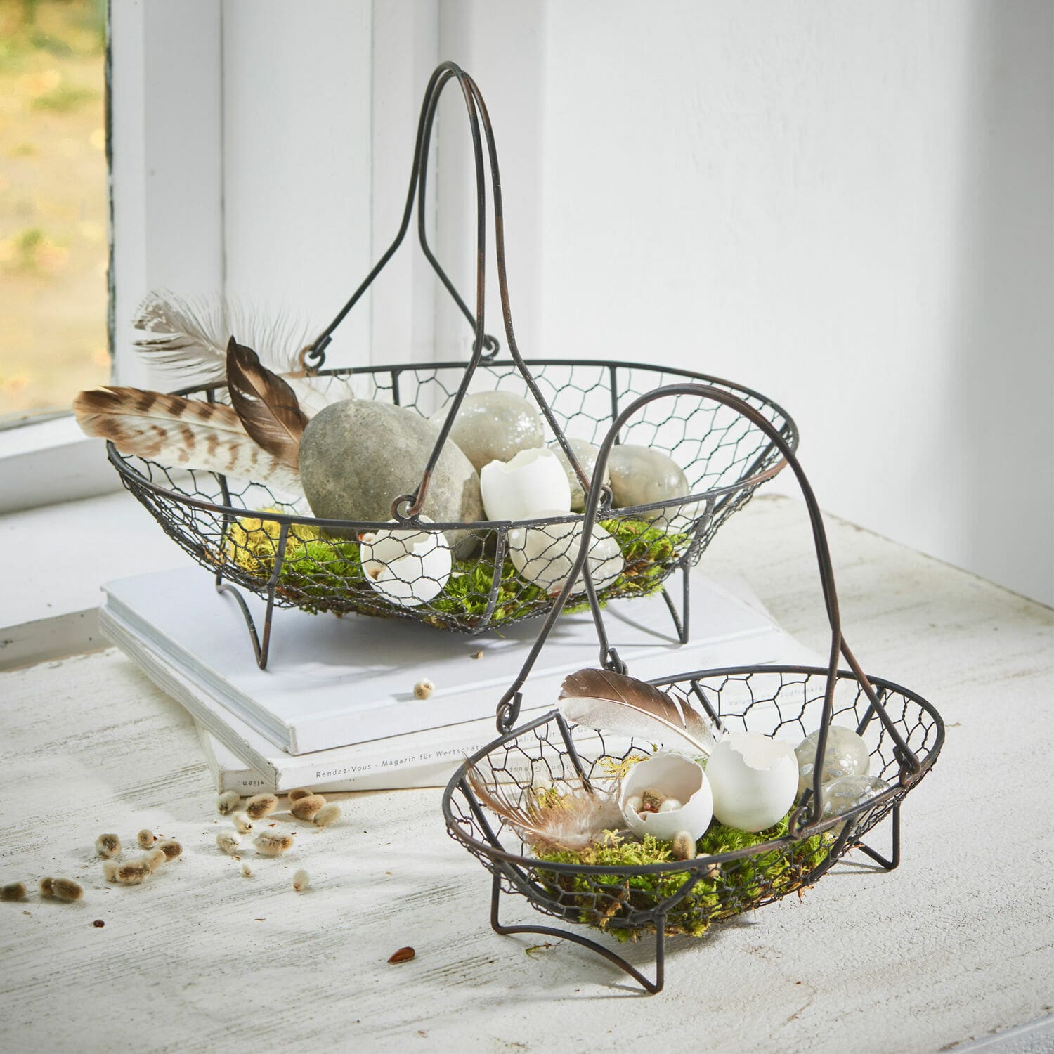 Set de 2 cestas Serrie Dos cestas metálicas negras con malla decoradas con conchas de huevo y plumas sobre musgo verde
