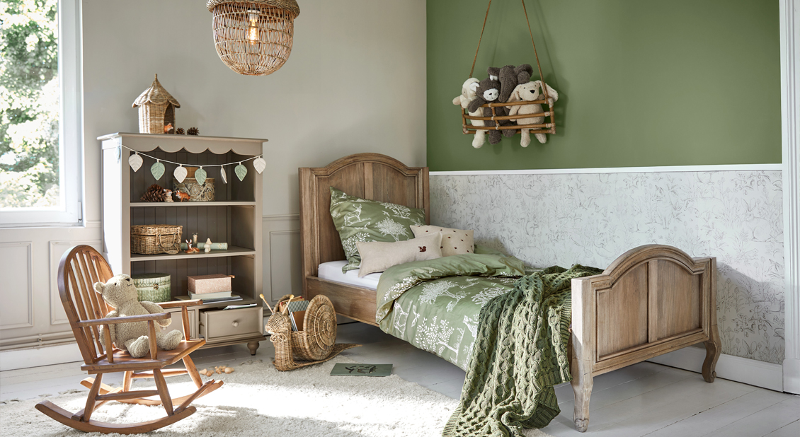 Cama infantil de madera con ropa de cama verde y peluches en habitación acogedora con decoración natural
