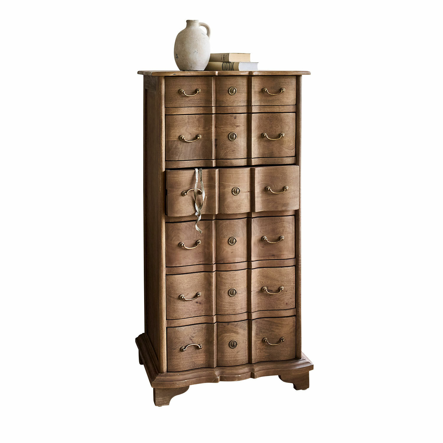 Cómoda Aiguillon Cómoda alta de madera natural con varios cajones y jarra de cerámica sobre libros