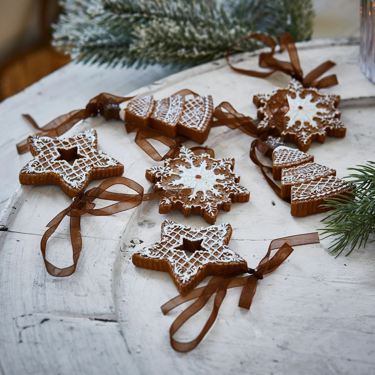 Set de 6 colgantes Chimayo Conjunto de adornos navideños de jengibre con glaseado blanco y cintas marrones sobre mesa de madera