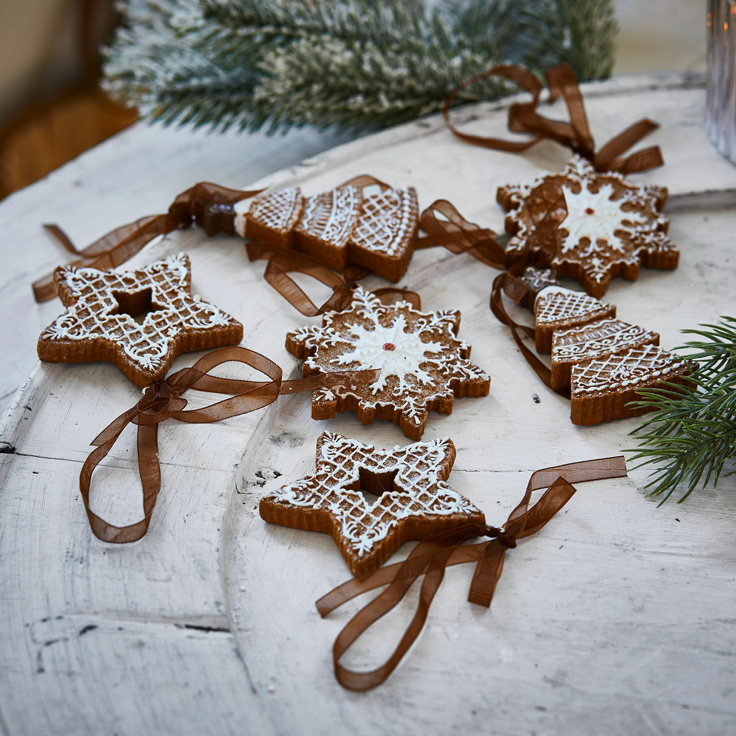 Set de 6 colgantes Chimayo Conjunto de adornos navideños de jengibre con glaseado blanco y cintas marrones sobre mesa de madera