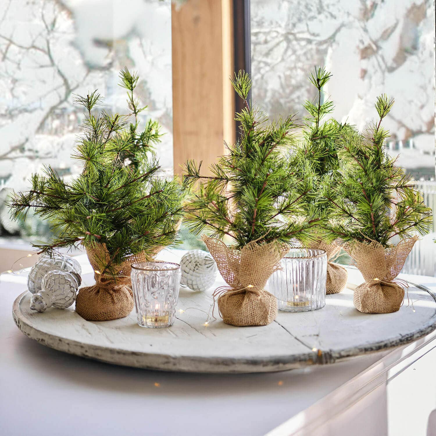 Set de 4 árboles decorativos Millies Pequeños árboles de Navidad decorativos en sacos de yute sobre bandeja blanca con velas y adornos navideños