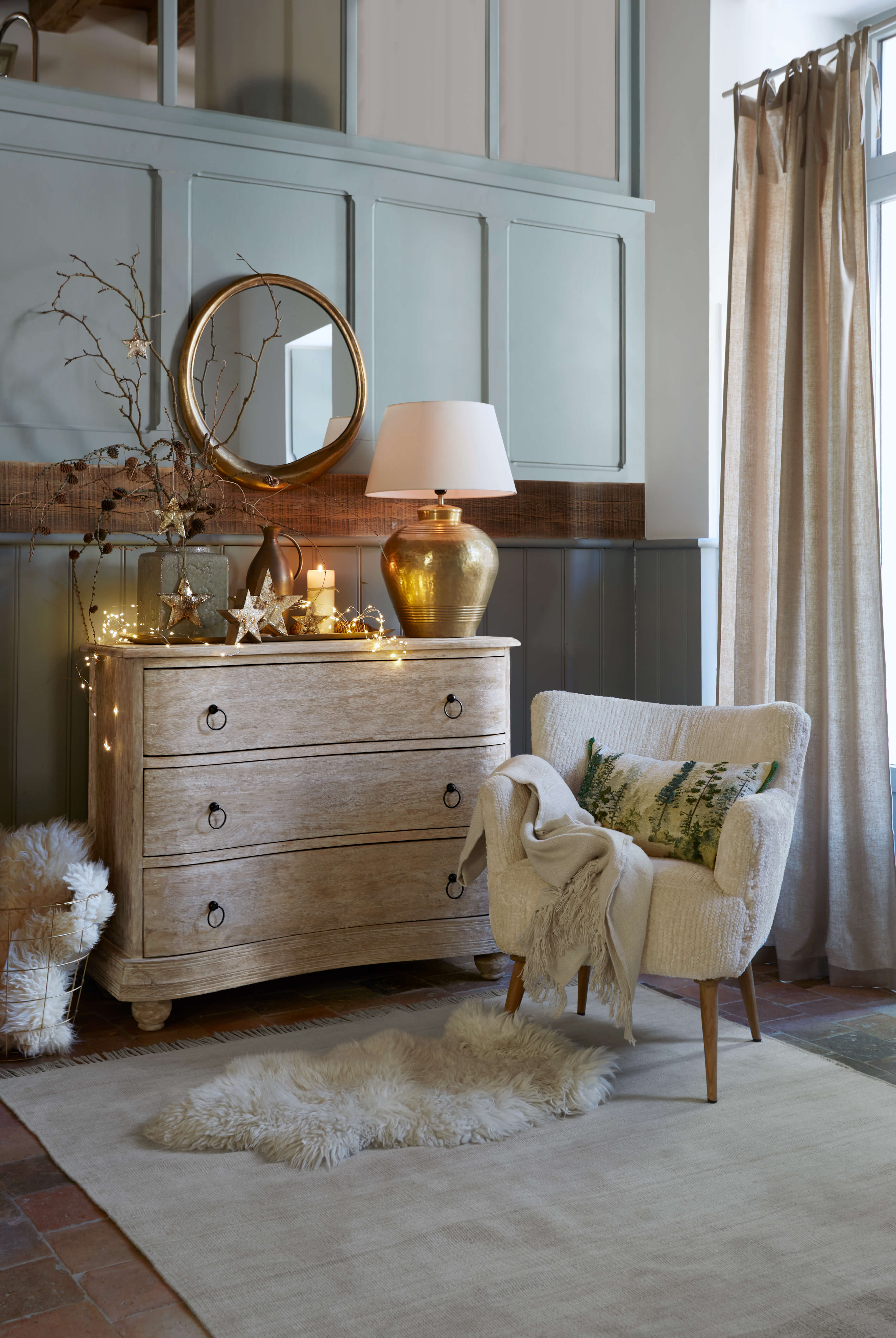 Rincón acogedor con sillón crema, cómoda de madera clara y lámpara dorada vintage en salón luminoso