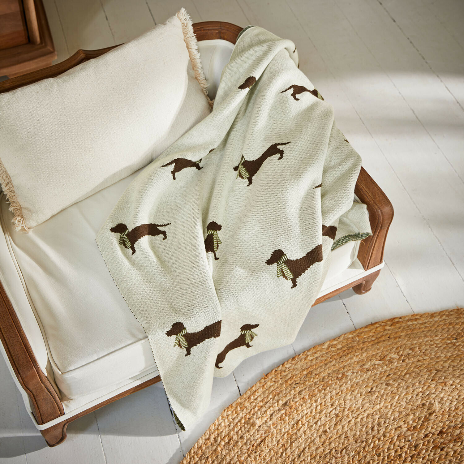 Manta para mascotas Brisette Manta beige con diseño de perro salchicha sobre sofá blanco de madera con cojín con flecos