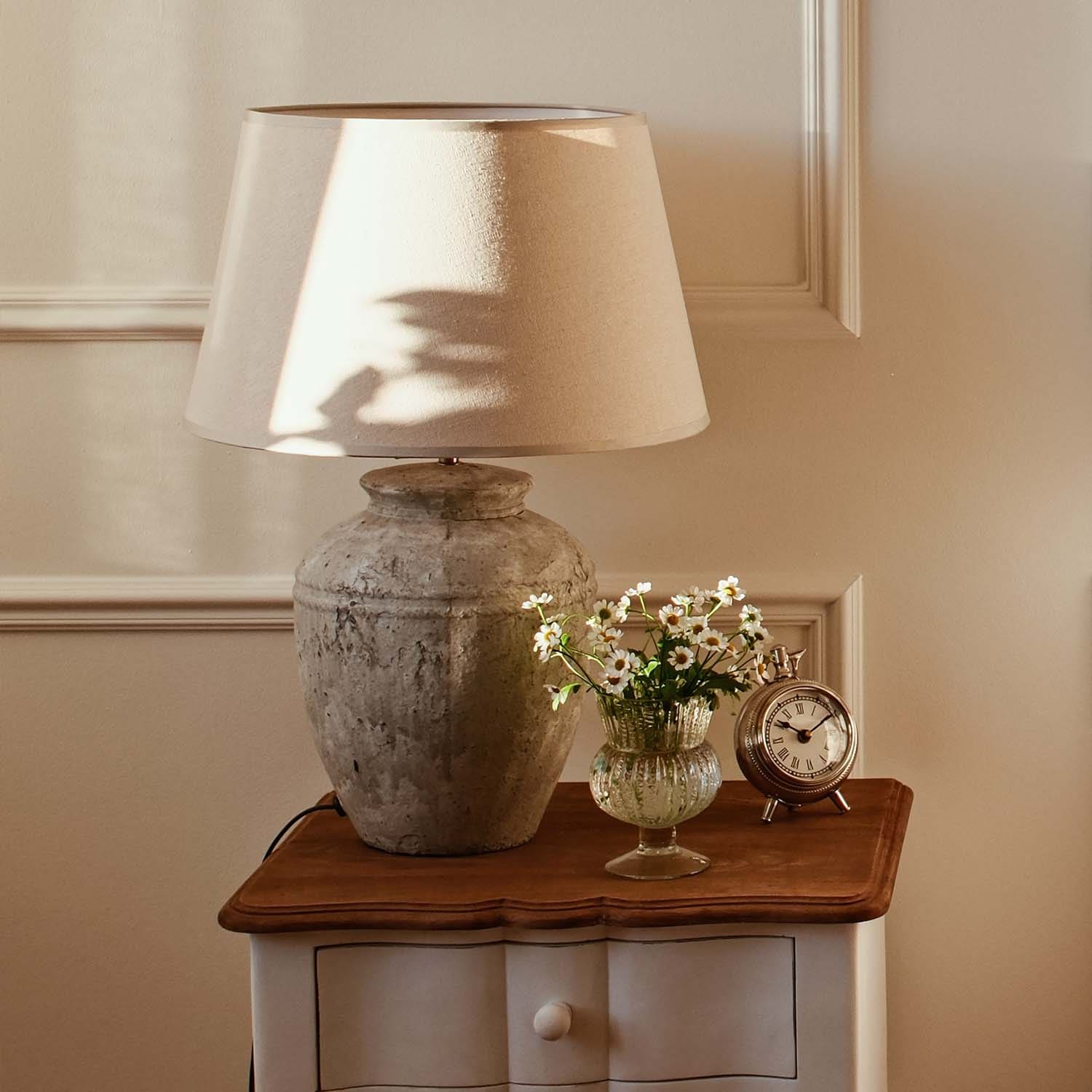 Lámpara de mesa con pantalla beige y base de cerámica vintage sobre mesa de madera con flores y reloj