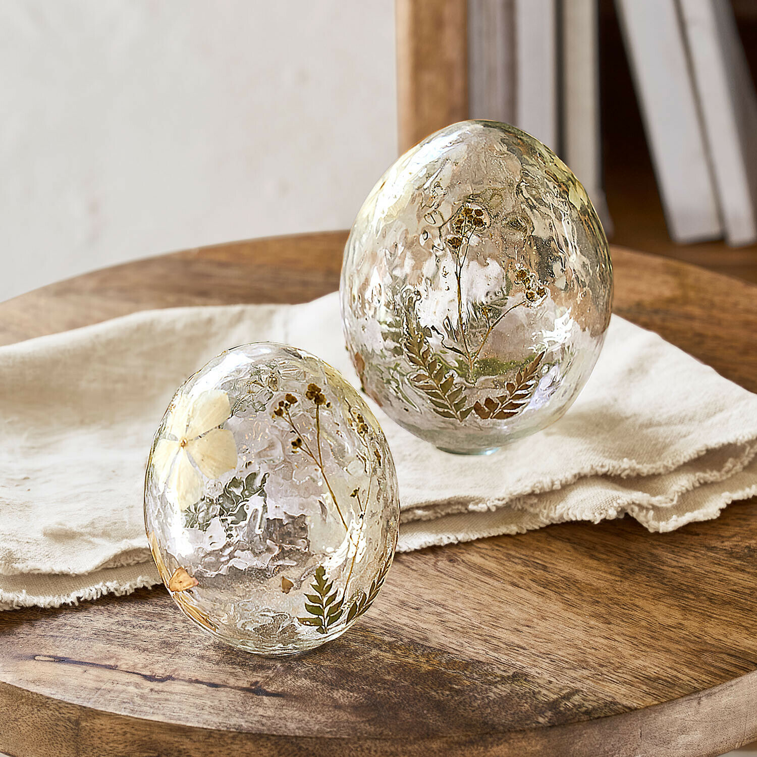 Set de 2 huevos decorativos Coudrisse Huevos decorativos de vidrio con flores secas y hojas incrustadas sobre mesa de madera