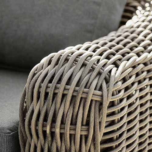 Detalle de reposabrazos trenzado marrón de material sintético en mueble de jardín con cojín gris