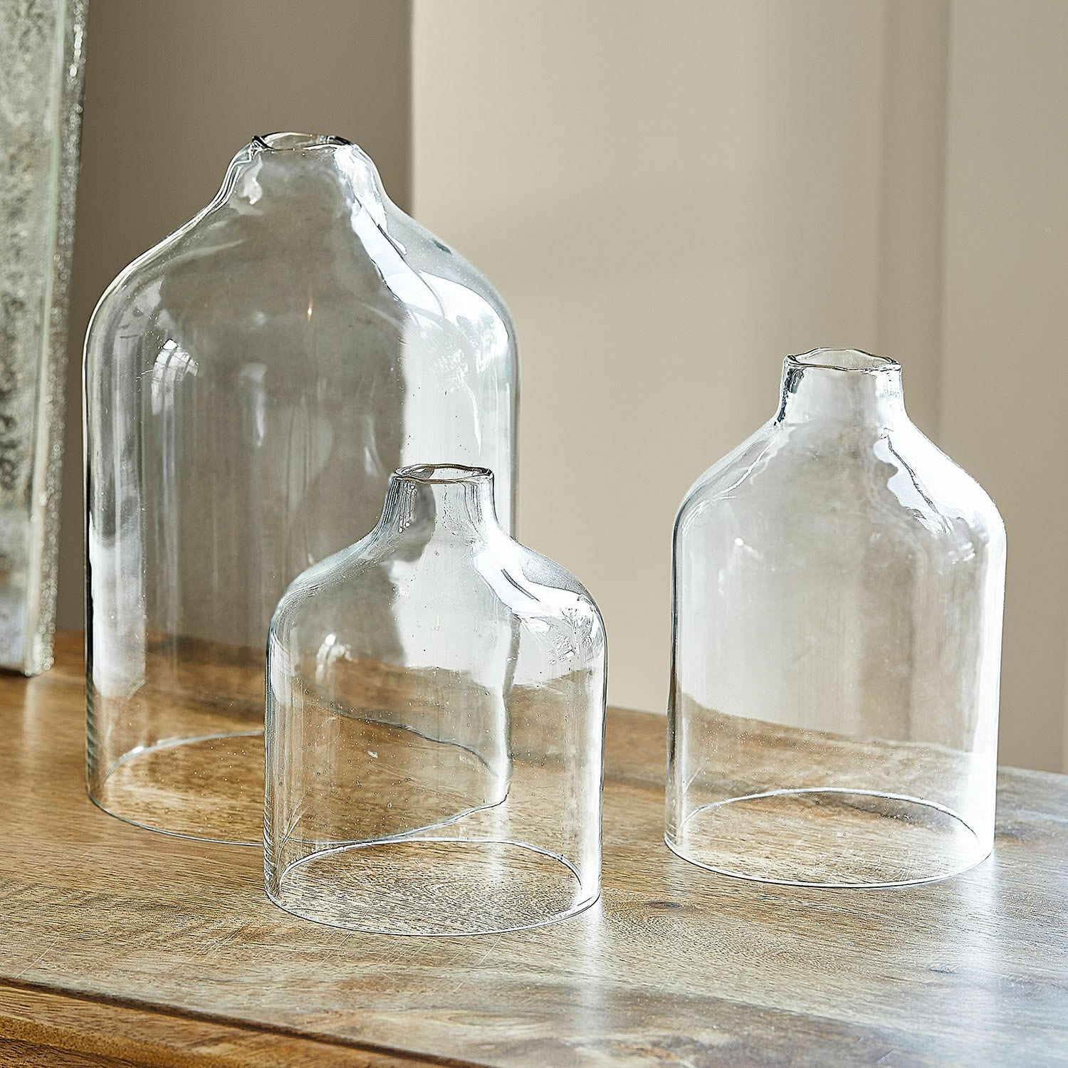 Set de 3 portavelas Xalvent Conjunto de tres jarrones de vidrio transparente de diferentes tamaños sobre mesa de madera